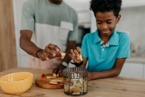 istock Young boy helps cut apples under supervision in kitchen. 2163218319