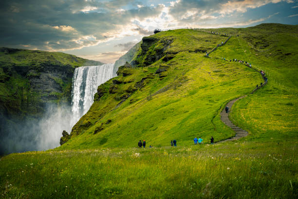Tourists walking up path with waterfall and green grass in iceland