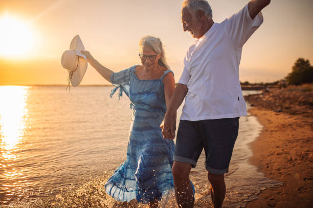 istock Joyful elderly couple splashing in beach water at sunset 2163223799