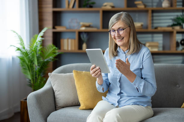 istock Senior woman enjoying a video call using tablet on a sofa at home with a smile 2163224228