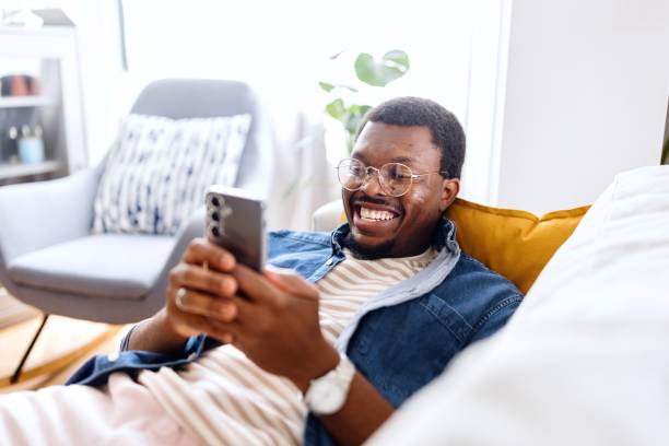 istock Black man lying on the bed and text messaging with someone 2163225415