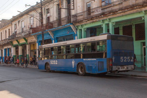 Havana, Cuba - June 2, 2024: A group of Cuban people wait for a public transportation bus to depart from a bus stop. Architecture of weathered buildings.
