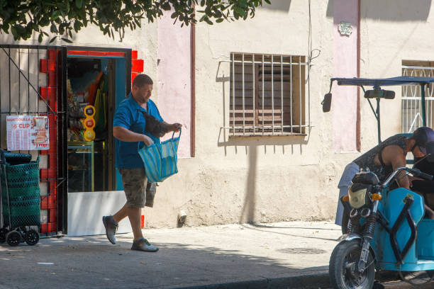 Havana, Cuba - June 2, 2024: A man leaves a small private business with a bag. He walks toward an electric tricycle waiting for him on the street.