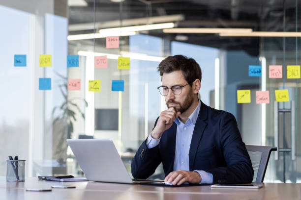 istock Businessman working on laptop in modern office with sticky notes on glass wall 2163234837