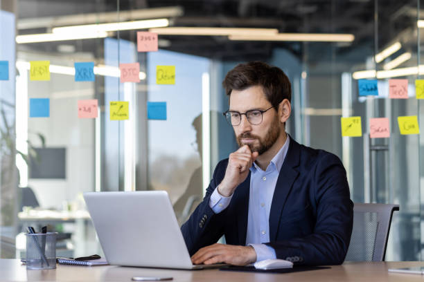istock Businessman working on laptop in modern office with sticky notes on glass wall 2163236278