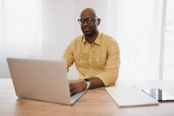 istock Smiling man working at desk with laptop and notepad. 2163236893