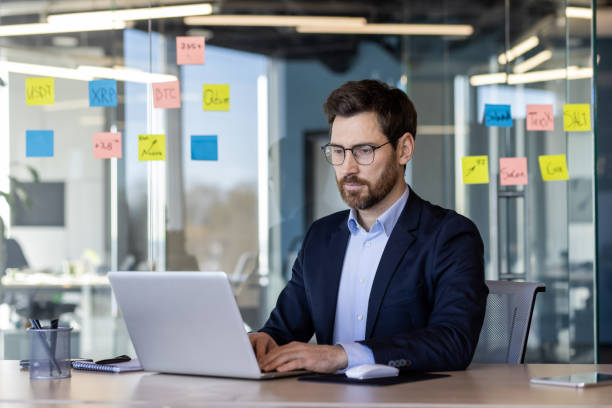 istock Businessman working on a laptop at modern office with sticky notes on glass wall 2163237888