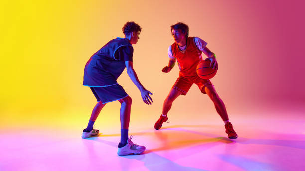 istock Two athletes practice basketball in vibrant lighting, displaying their agility and dedication in neon light against gradient studio background. 2163238645