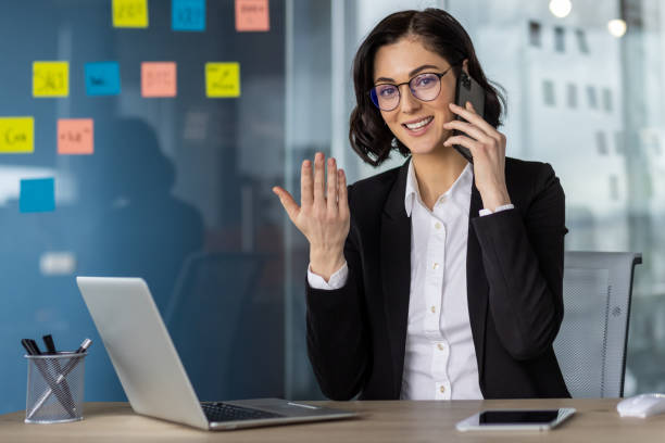 istock Confident businesswoman using phone and laptop in modern office workspace 2163240957