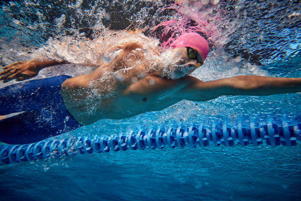 istock Focused swimmer, seen from below, cutting through water with strong freestyle stroke, wearing blue trunks and goggles. 2163243980