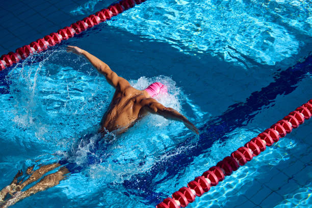 istock Swimmer in pink cap executes powerful butterfly stroke, his muscular form cutting through blue water, creating dynamic splash between red lane dividers. 2163244078