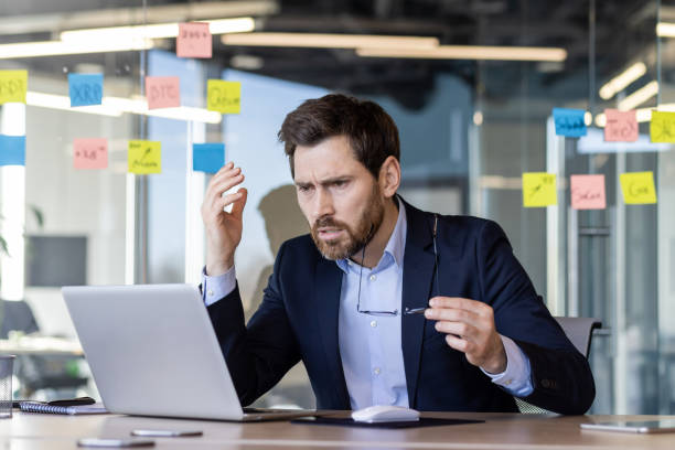 istock Stressed businessman working on laptop in modern office with sticky notes in background 2163244523