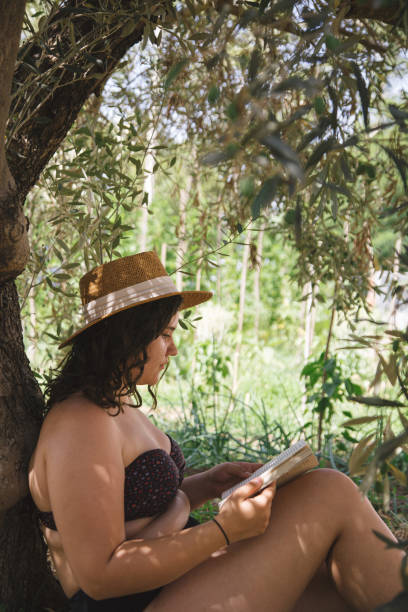 istock Young woman reading book under olive tree 2163244632