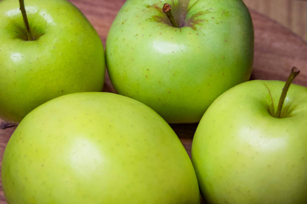 istock Four green apples with stems, glossy finish, on a dark surface. The image conveys freshness and is ideal for health food promotion. 2163247115