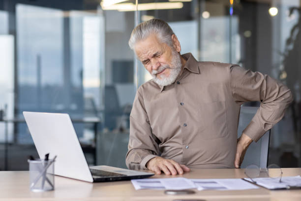 istock Elderly man experiencing back pain while working at office desk with a laptop 2163247342