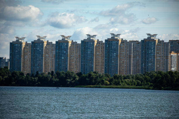 Skyscrapers adorned with unique rooftop sculptures stand by a peaceful waterfront, enveloped in lush greenery