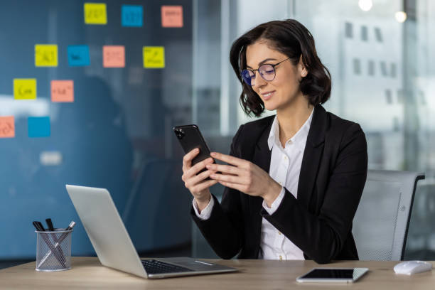 istock Businesswoman using smartphone at modern office with laptop, working and multitasking 2163253050
