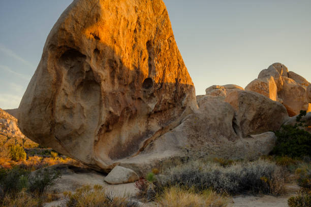 The sun sets on boulders, rocks and desert grass, lighting uo the rocks in a golden hue.