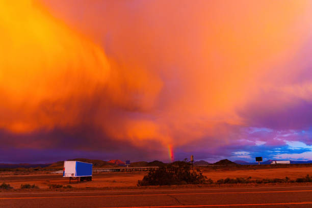 Stunning sunset in California desert, showcasing vibrant orange and purple hues in the sky. A rainbow peeks through the clouds, creating a breathtaking contrast with the landscape.