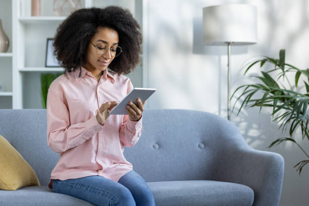 istock Woman using tablet while sitting on couch in modern living room 2163261150