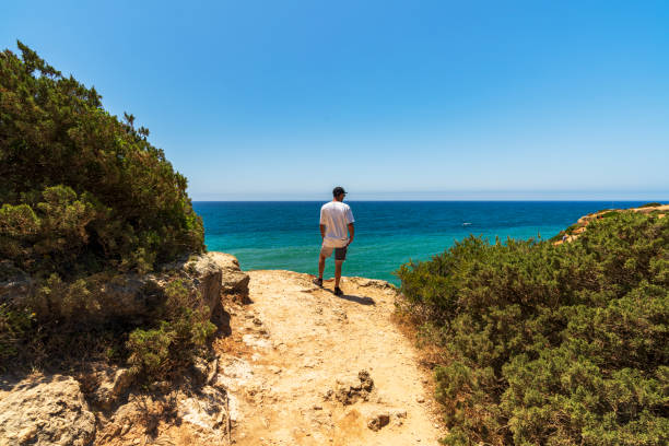 Rear view of a man on top of a cliff overlooking the ocean, Algarve