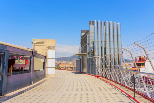 Barcelona, Spain - July 16, 2024: Contemporary rooftop area featuring modern design elements, including an outdoor dining space and industrial structures, overlooking scenic Barcelona skyline.