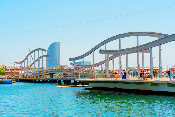 Barcelona, Spain - July 16, 2024: Contemporary bridge over marina with famous tower in Barcelona port