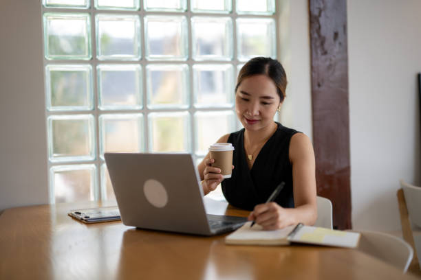 istock Smiling Woman Enjoying Coffee While Working on Laptop 2163278836