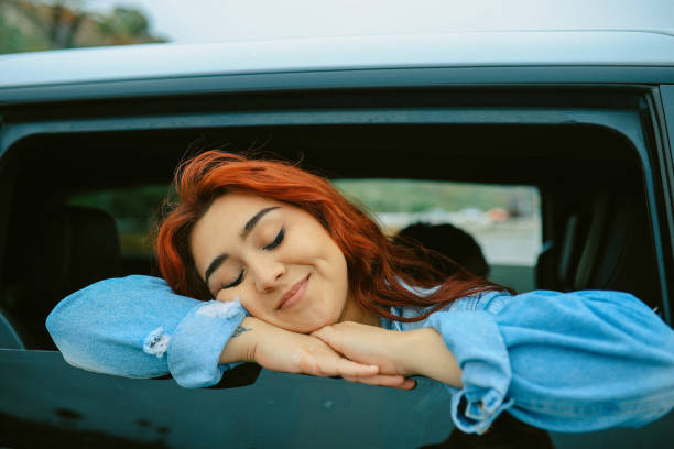 Tired young woman driver asleep on pillow inside her car, resting after long hours driving. Fatigue. Sleep deprivation.