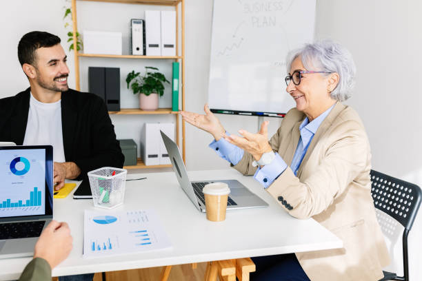 Diverse business people talking at workplace while working on laptop in the office