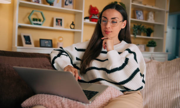 istock Beautiful happy confident woman in eyeglasses working on comfortable couch, using laptop at home, happy girl chatting with friends in social network, watching movie, shopping online, freelancer 2163306021