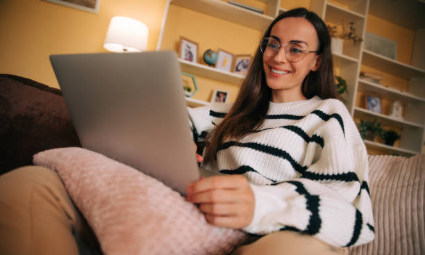 istock Beautiful happy confident woman in eyeglasses working on comfortable couch, using laptop at home, happy girl chatting with friends in social network, watching movie, shopping online, freelancer 2163306102