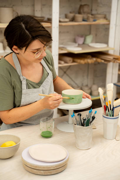 istock Using a brush to paint a ceramics bowl. Learning how to paint a handmade pottery project. Girl is decorating a clay product with bright green color. 2163311440
