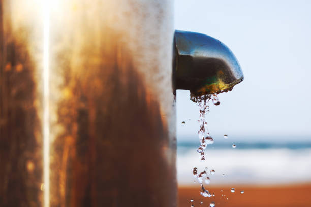 Water is falling from a faucet on the beach. Metal pipe is dripping water