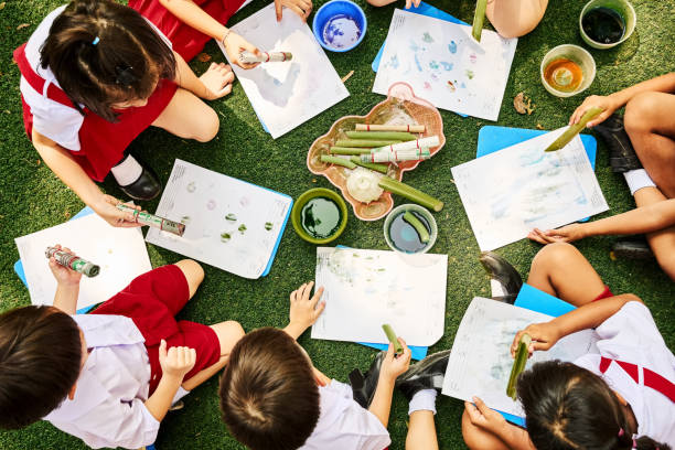 Children sitting in circle doing stamp painting with objects at school