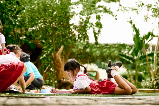 Small girl lying on the grass and drawing during an outdoor activity class at the schoolyard