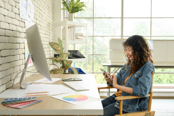 istock Asian female graphic designer talking on mobile phone with colleague or customer while working in office. 2163349947