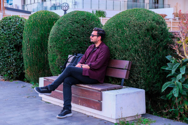 A middle-aged or senior man relaxes on a park bench looking at a clear blue sky.