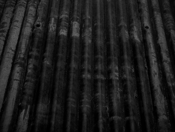 Black coloured grunge textured blank empty corrugated metal tin or iron background or wallpaper with zigzag wavy curvy parallel rows of pattern of curved lines as three dimensional design all over. Can be used as elegant classy party celebrations backdrop wallpaper, greeting cards, background or gift wrapping sheet.