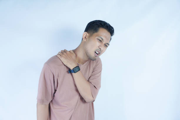 istock A man in a pink shirt holds his shoulder with a pained expression, indicating shoulder pain or discomfort. The plain light blue background emphasizes his distress 2163364191