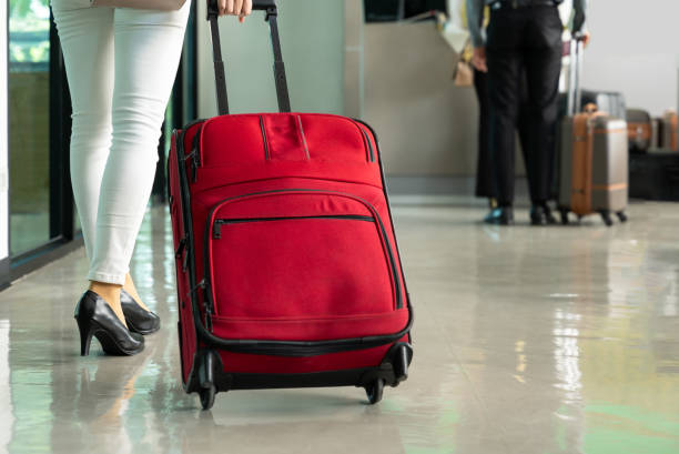 istock Woman passenger pulling large red suitcase walking in airport terminal. 2163364204