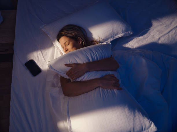 High angle view of relaxed woman embracing her pillow while sleeping in bed at night. Photographed in medium format.