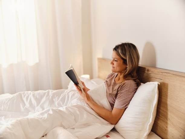 istock Smiling woman reading a book in a bed. 2163370247