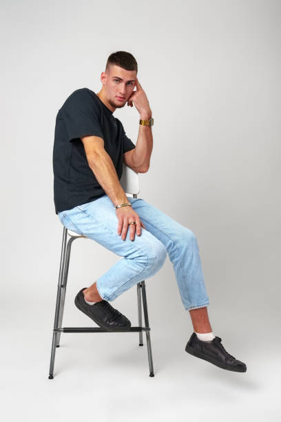 istock Young Man Sitting on a Stool Against a White Background 2163370723