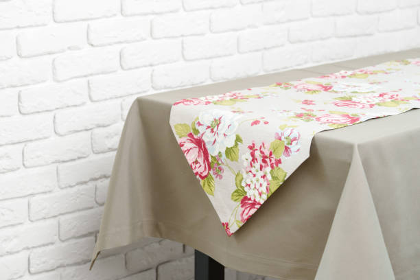 istock Floral Table Runner on a Beige Tablecloth Against a White Brick Wall 2163371966