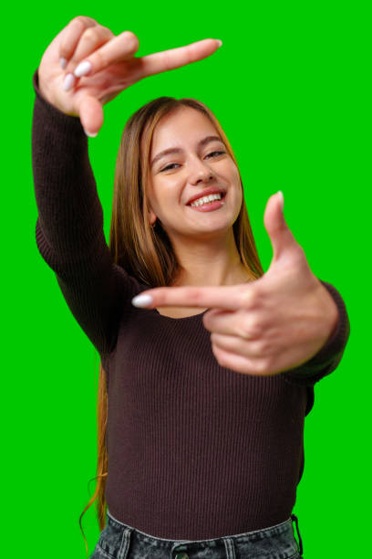 istock Smiling Woman Making Framing Gesture in Front of Green Screen 2163372326