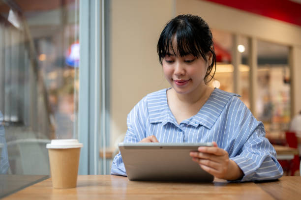istock A charming young Asian woman using her digital tablet at a table in a coffee shop, working remotely. 2163373788