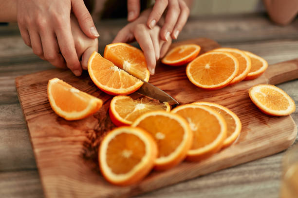 Hands expertly slicing fresh oranges on a wooden cutting board in a cozy kitchen