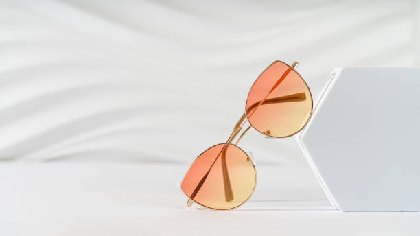 istock Woman's sunglasses with color lenses in metallic frame on a podium on a white background. Trendy sunglasses still life, minimal style. Optic store discount banner, sale, promotion. Copy space 2163393221