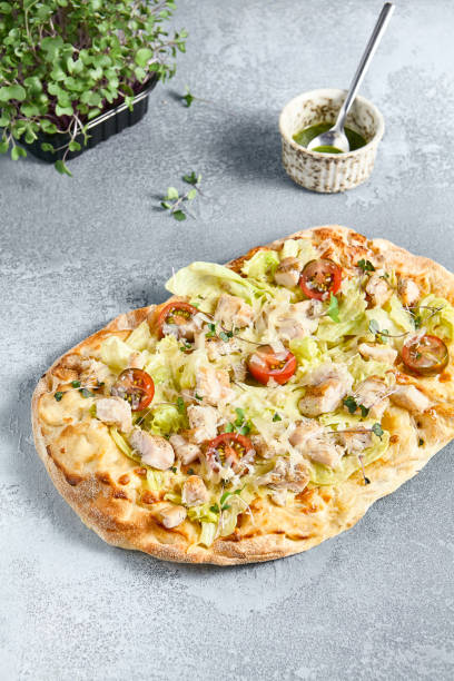 istock Caesar Pinsa with Chicken Fillet and Cherry Tomatoes on Rustic Grey Surface 2163400128